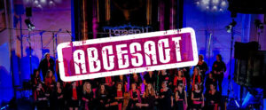 Der Grazer Gospelchor steht im Mittelpunkt der Bühne auf einer schwach beleuchteten Plattform, leuchtende Lichter tanzen um ihn herum, während die auffällige Grafik „ABCESACT“ über der fesselnden Darbietung schwebt.